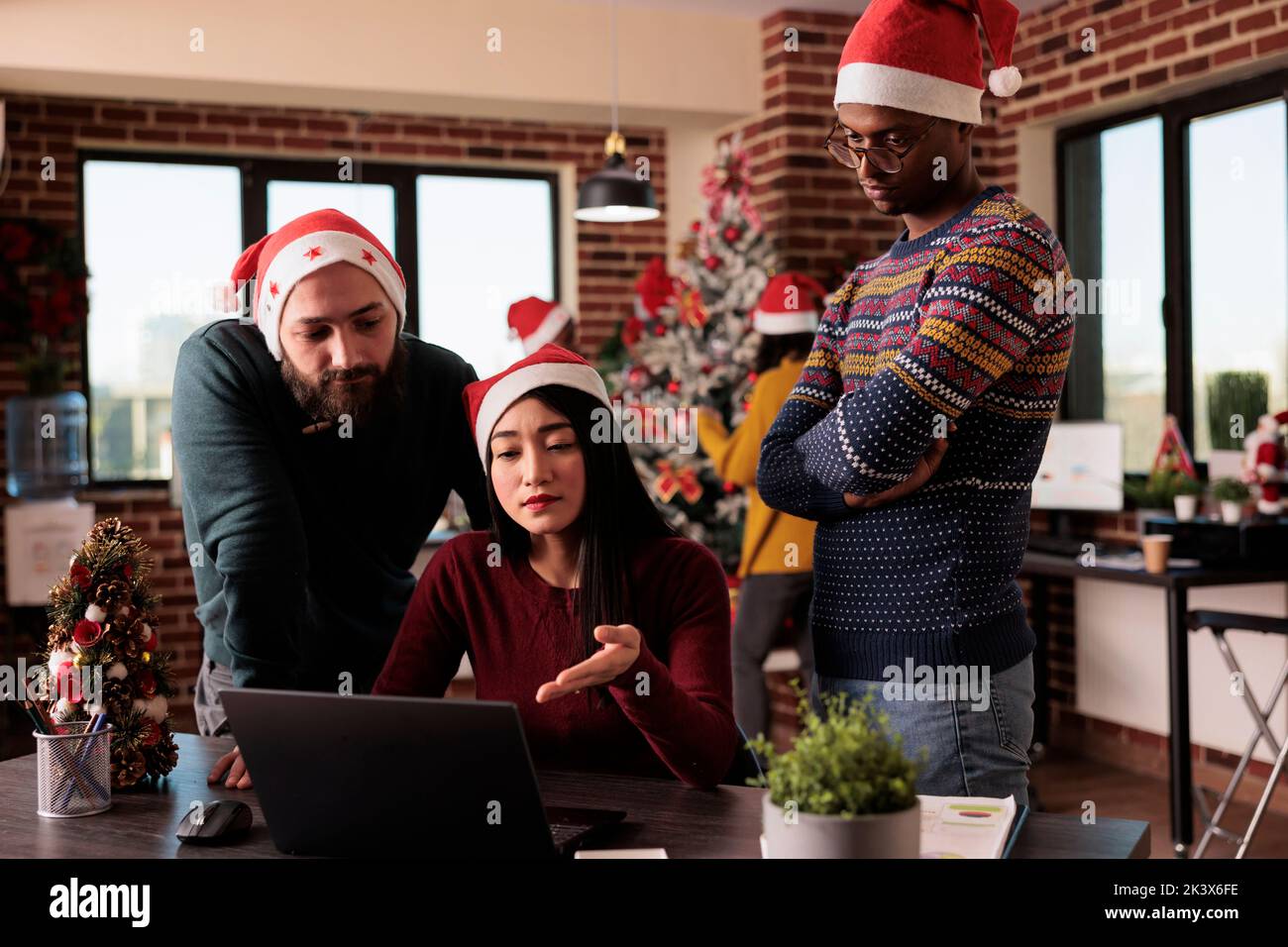 Diverse group of people working during christmas eve, doing teamwork to plan business project in office with xmas lights and festive decorations. Using laptop at job, seasonal winter holiday. Stock Photo
