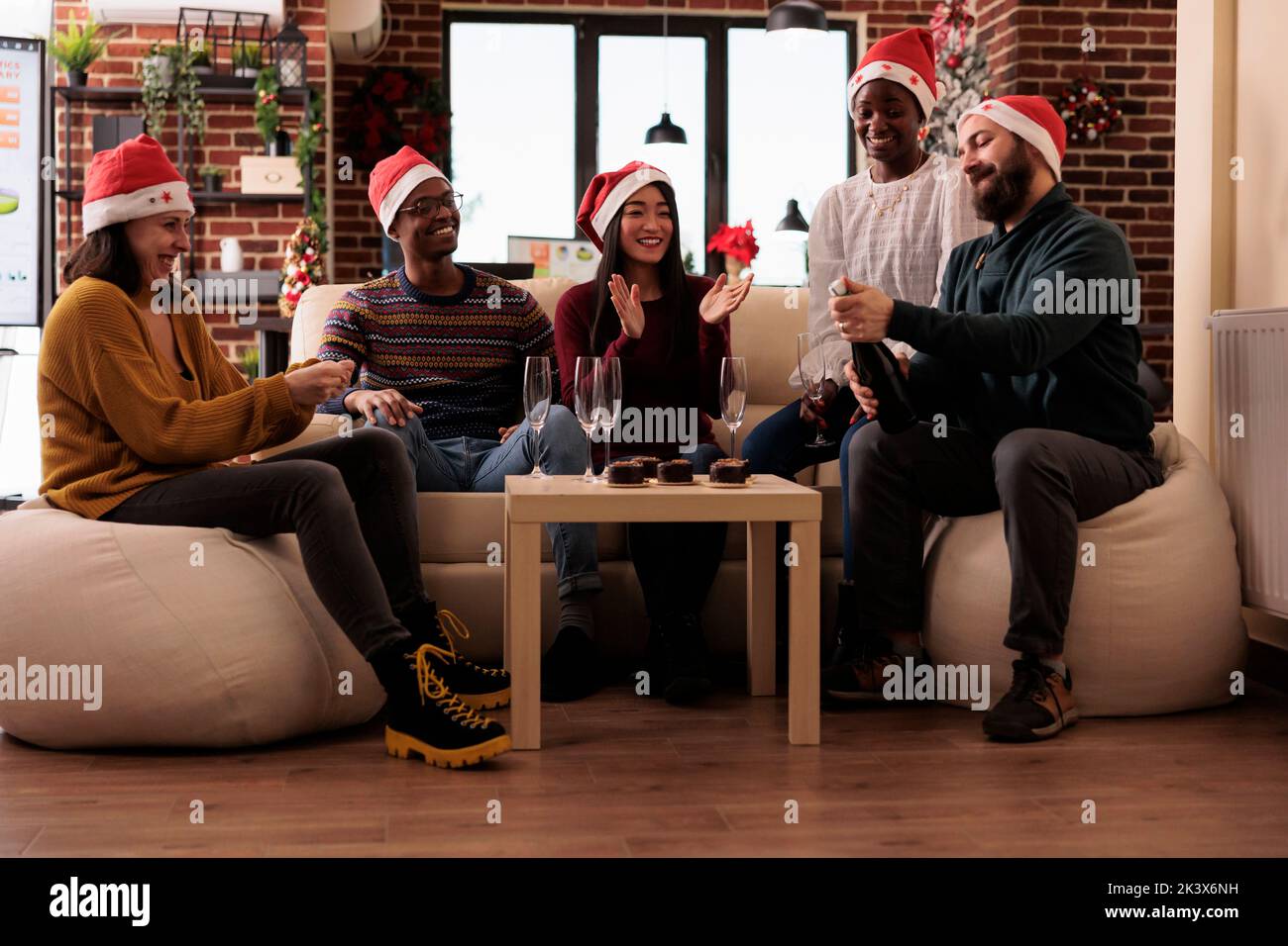 Diverse coworkers celebrating christmas at job party, drinking wine in glasses and having fun on winter holiday season. Festive office with xmas tree and seasonal decor, alcohol drink. Stock Photo