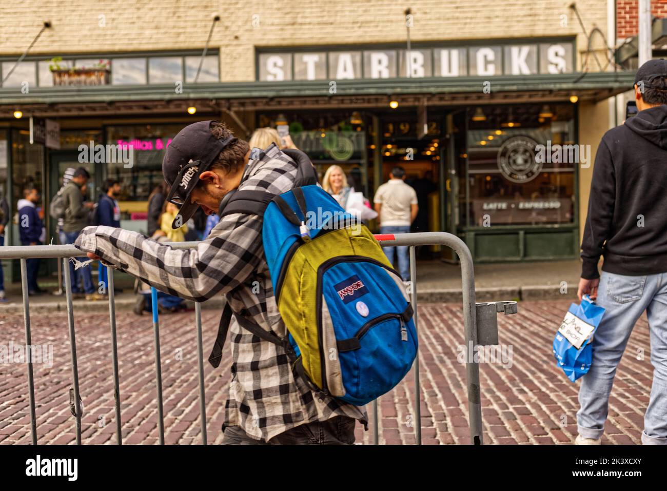 A Junky man wearing backpack and catching a fence in Seattle Street Stock Photo