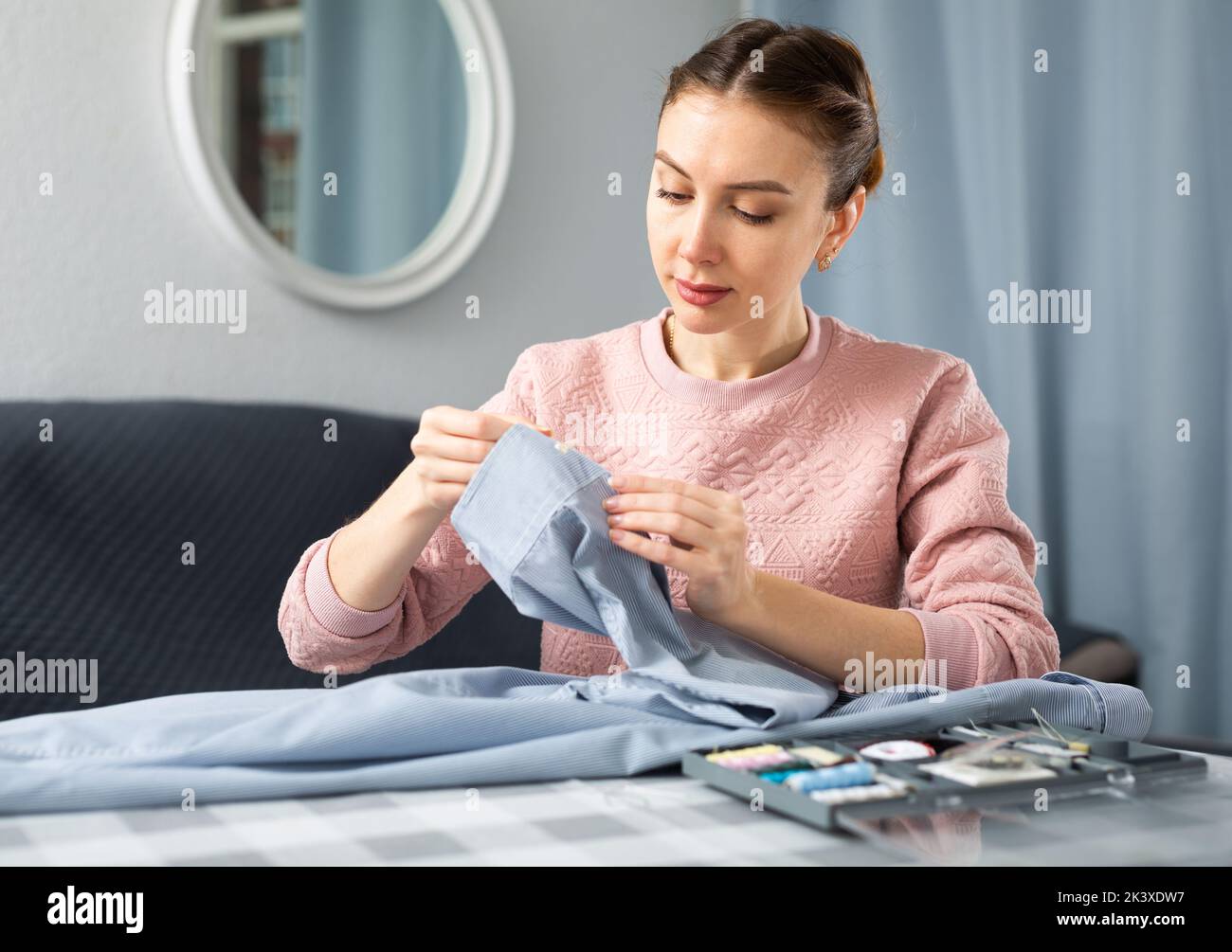 Young woman sewing on button at home Stock Photo - Alamy