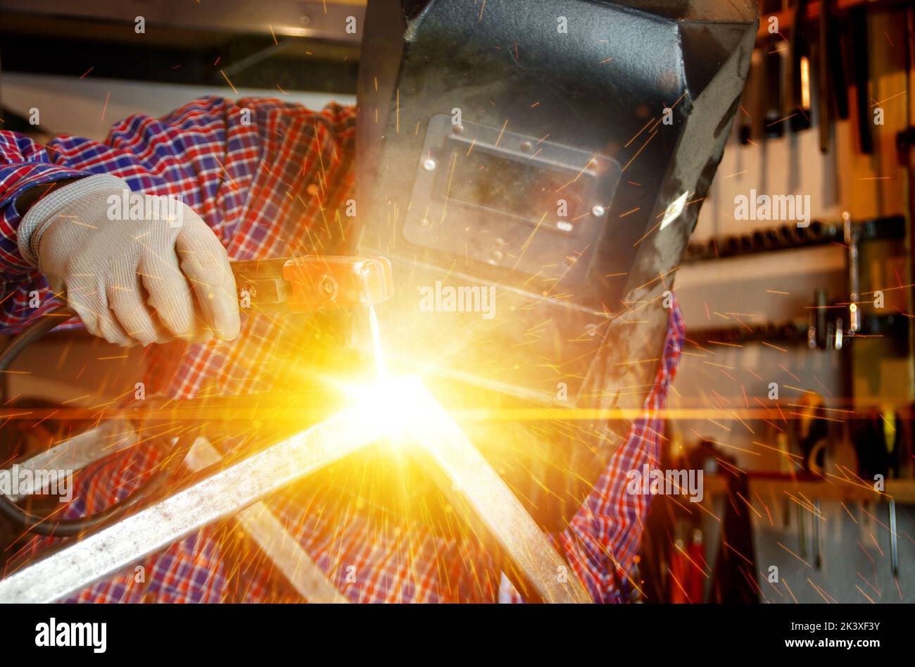 Welding of metal construction with flash light and sparks. Welder man in work. Locksmith with an electrode in hand. Metalwork production factory. Heav Stock Photo