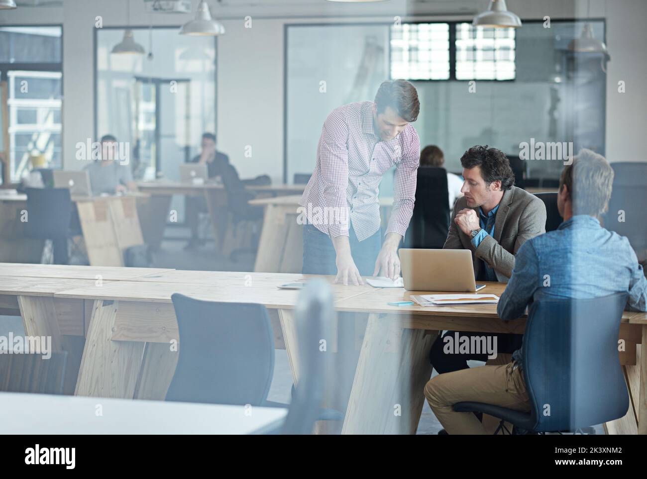 Getting down to business. Through the glass shot of a group of colleagues working together in an office. Stock Photo