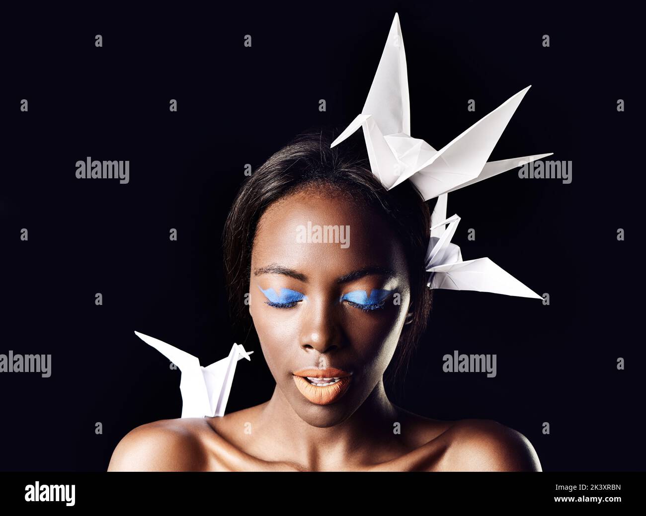 Shes a true queen. a beautiful ethnic woman posing with origami birds on her head and shoulders. Stock Photo
