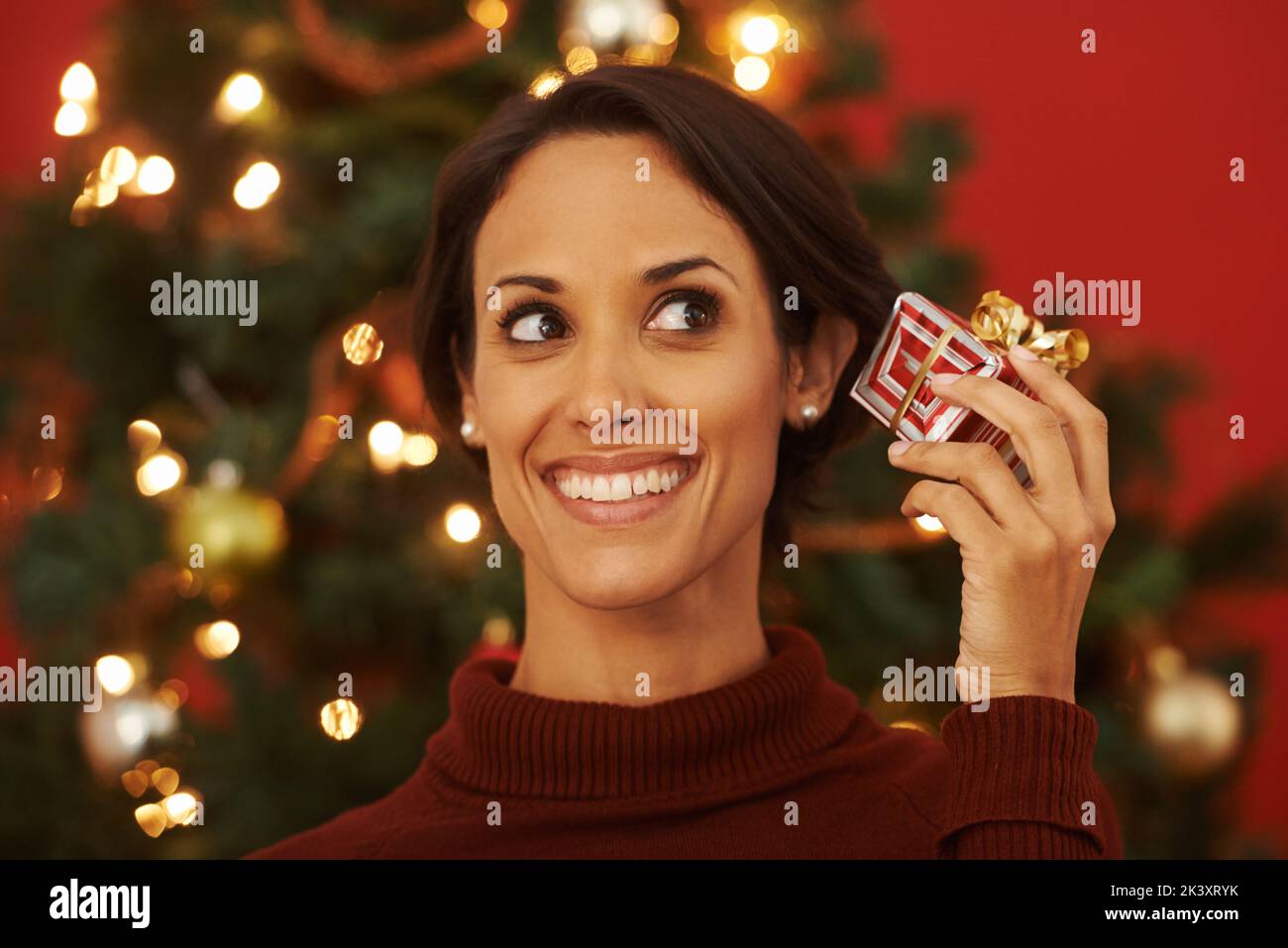 I hope its what I wanted. an attractive young woman holding a present while standing by a Christmas tree. Stock Photo