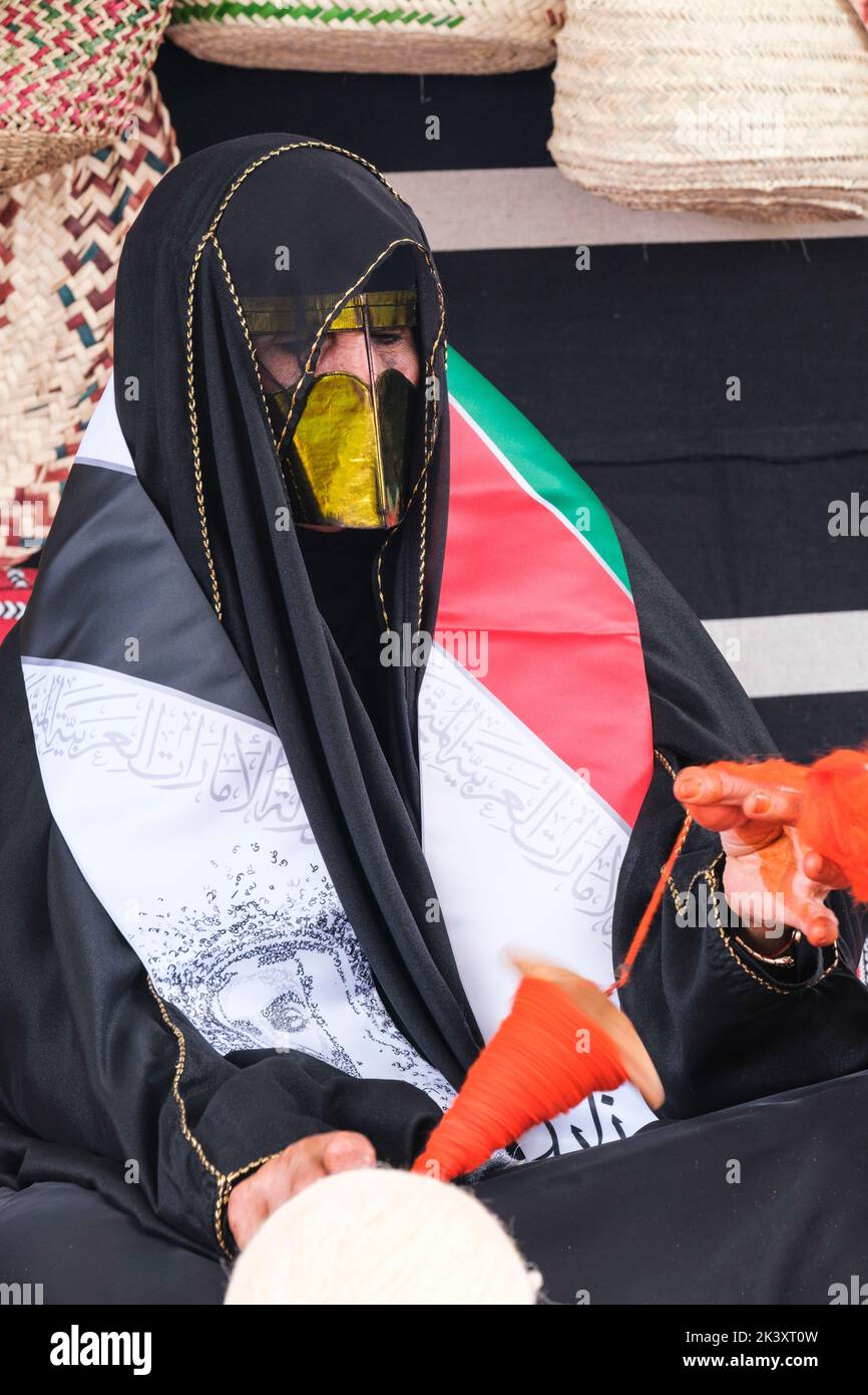Masked Arab Woman from Abu Dhabi Wearing an Abaya at a Folklife Festival Demonstrating Traditional Handicraft Skills,  Putting Wool on to a Spindle. Stock Photo