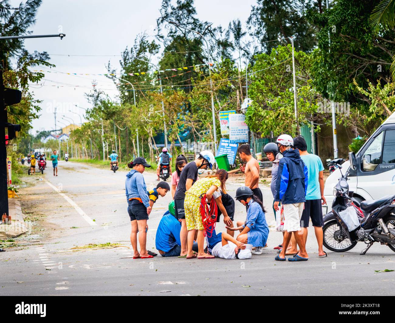 Motorbike accident with people attending a male that is on the ground at big intersection of An Bang Beach, Vietnam. Stock Photo