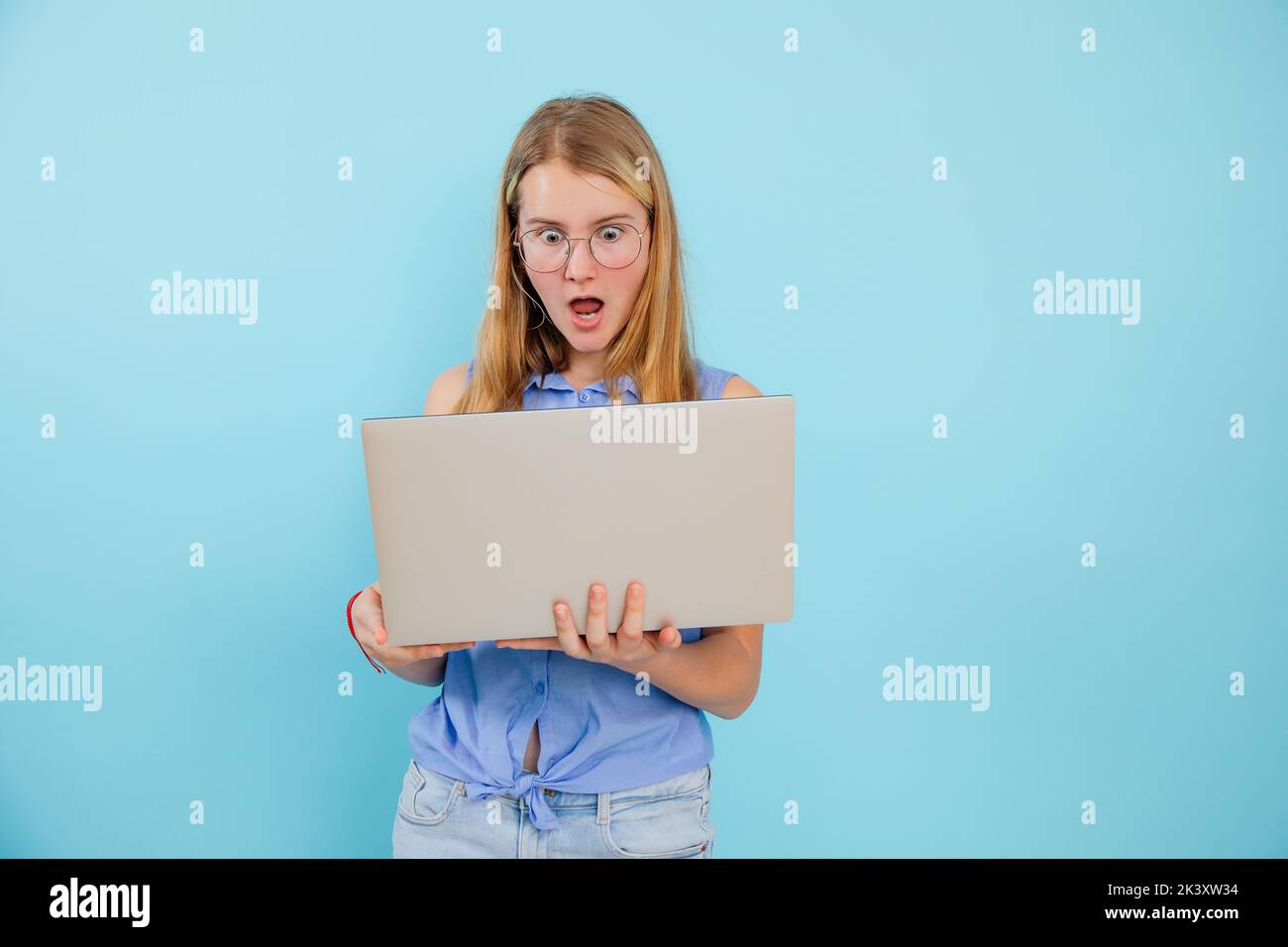 Portrait of surprised teenage girl wearing blue shirt, glasses, holding ...