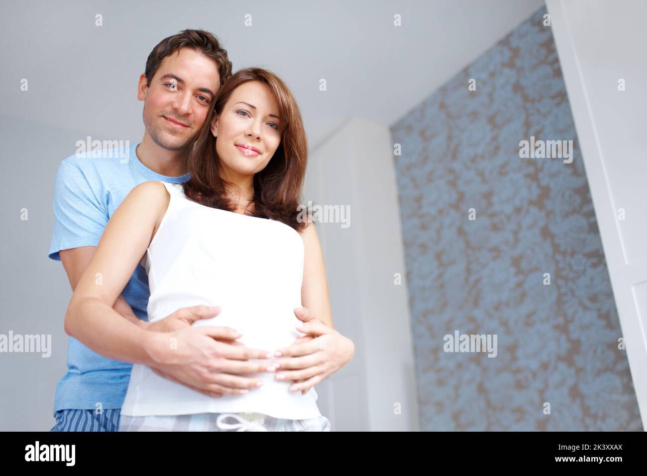 Committed parents to be. Young man holding his girlfriends pregnant belly as they look at you. Stock Photo