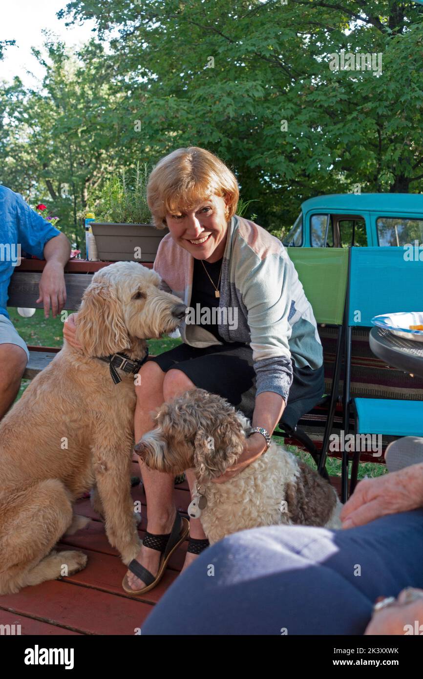 Woman trying to pet two dogs at the same time on a cabin deck. Clitherall Minnesota MN USA Stock Photo