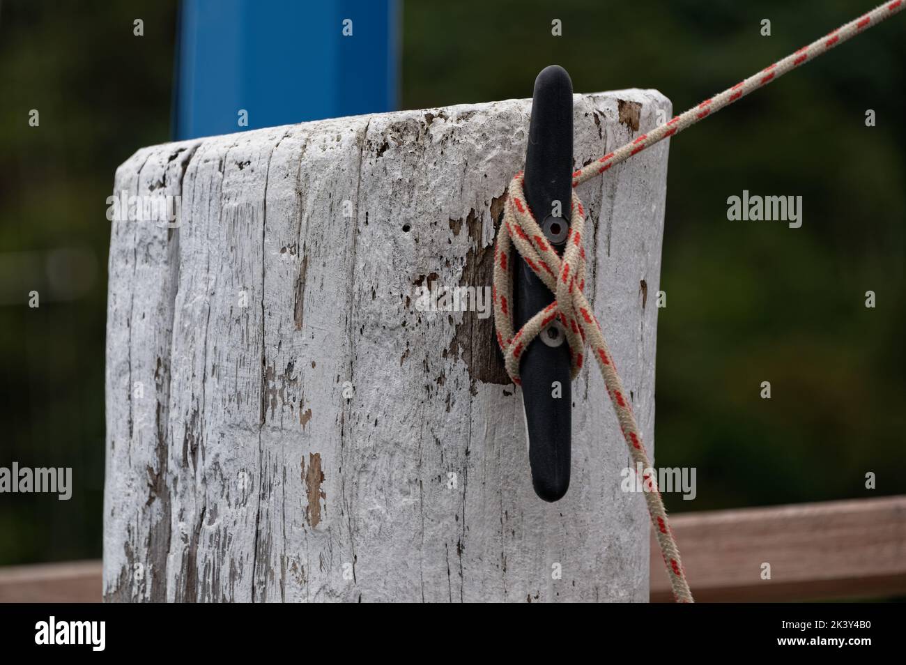 A red and white rope is tied around a cleat on a post at a wharf to keep a boat secure. Stock Photo