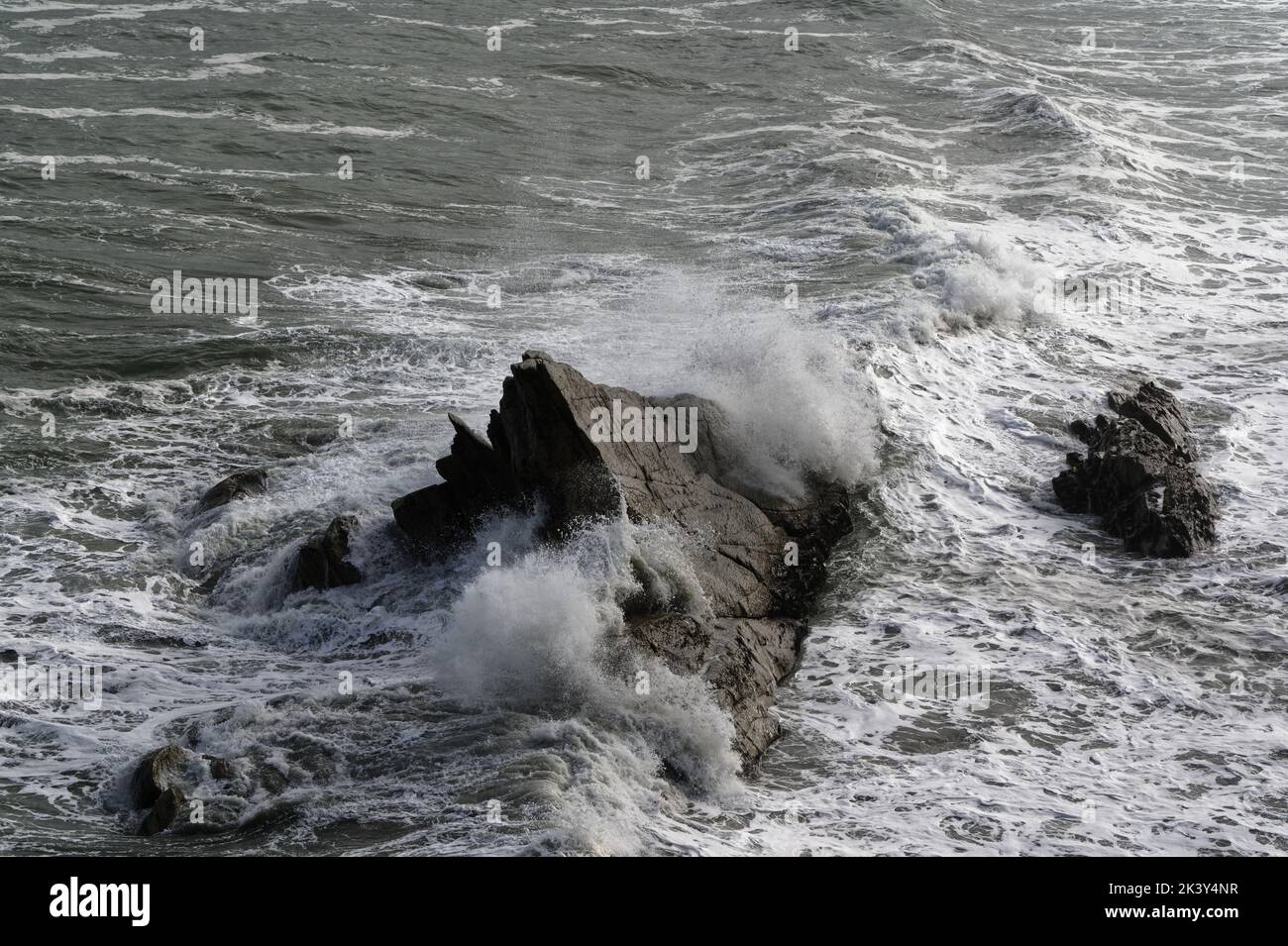 The sea churns around rocks in the ocean as waves surge forward. Stock Photo