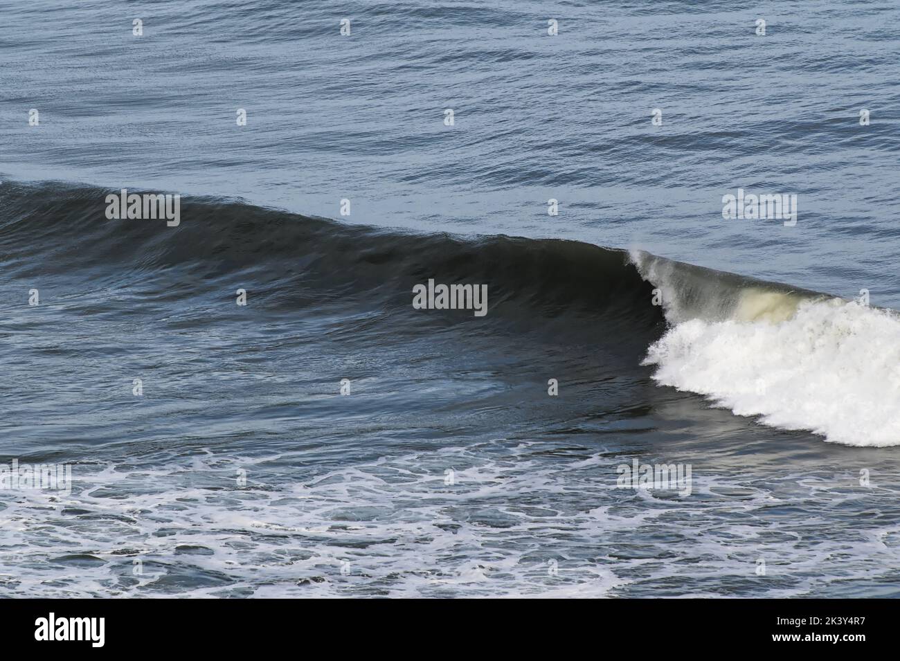 Wave crests then rolls down the face of the wave, throwing spray off the top. Stock Photo