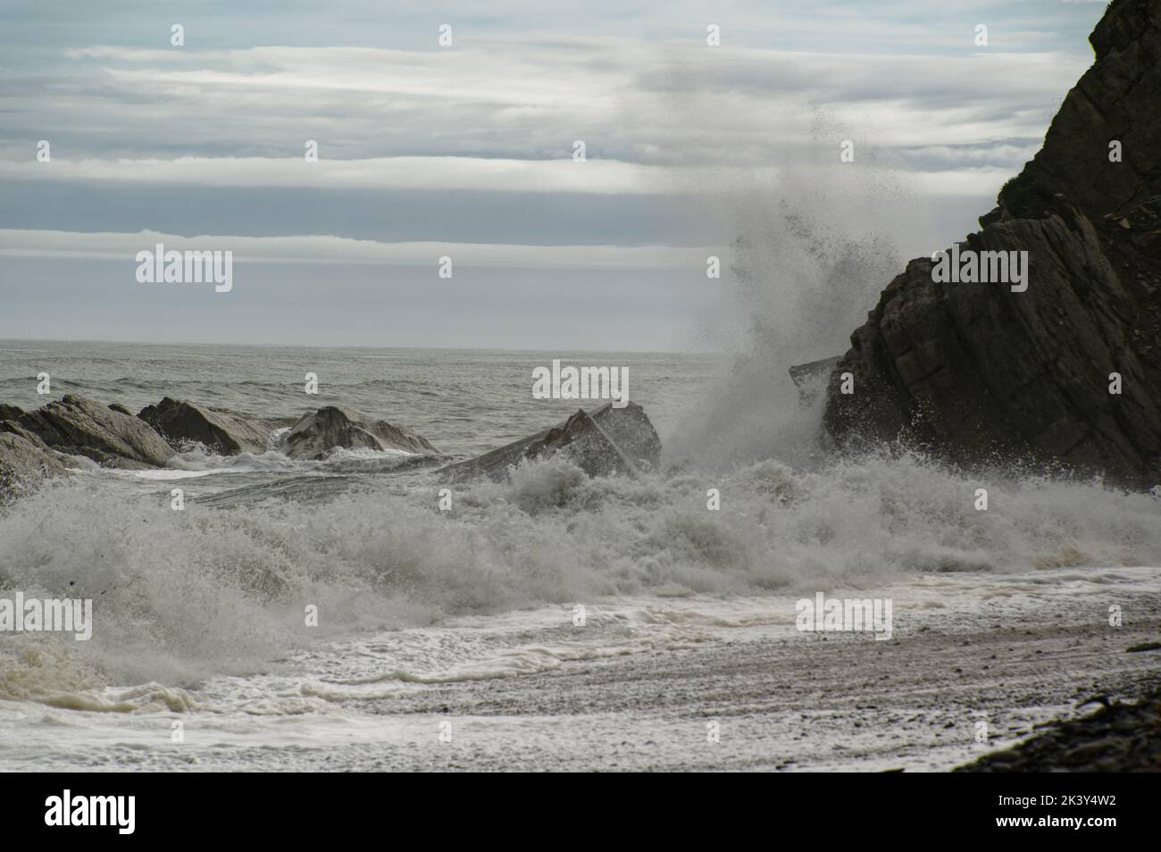 A stony beach has a rocky end with waves crashing against it Stock Photo
