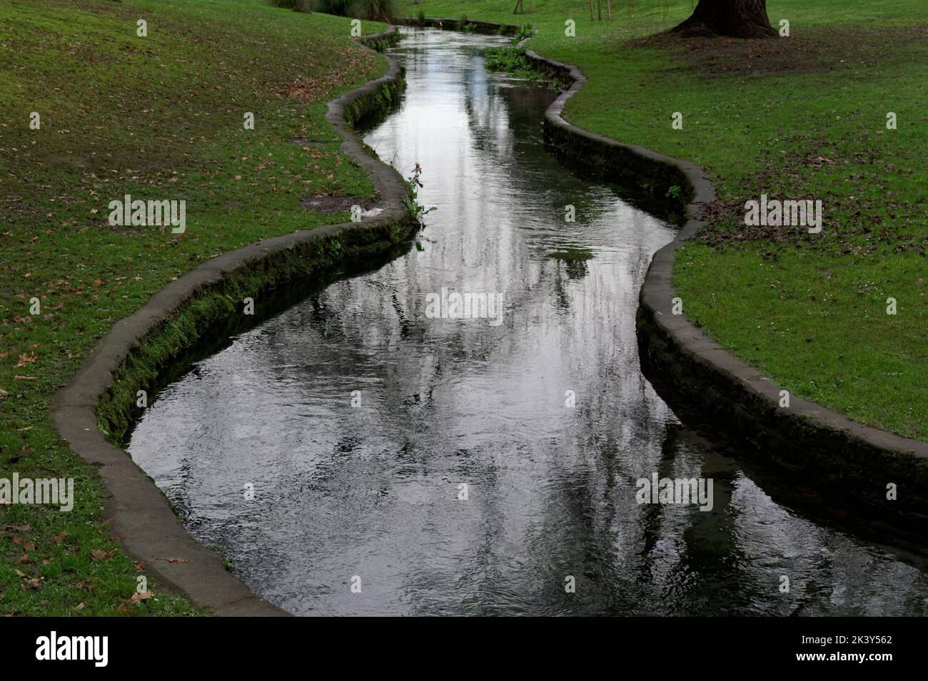 A stream has been contained by concrete sides to ramble through a public park Stock Photo
