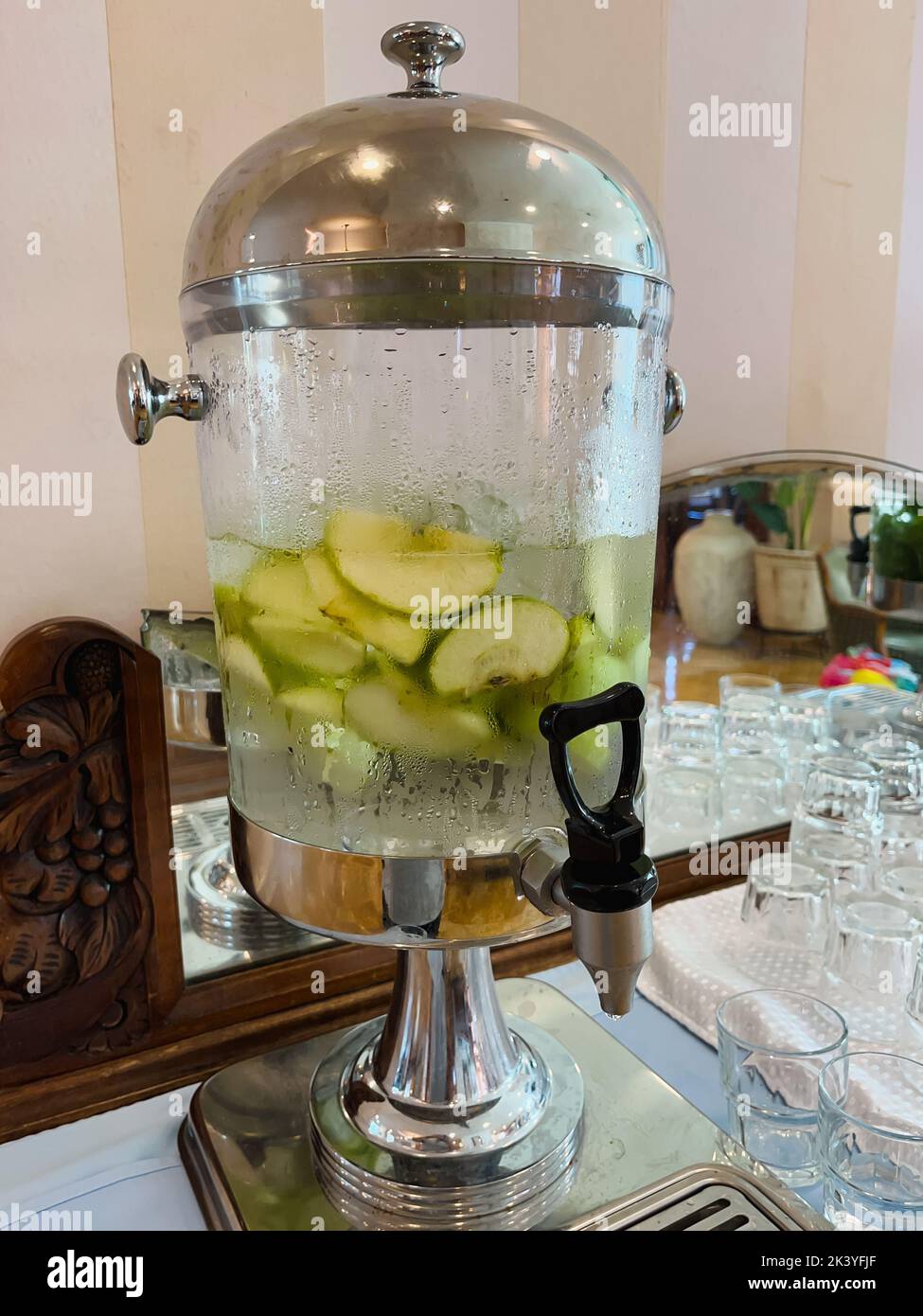 https://c8.alamy.com/comp/2K3YFJF/a-glass-transparent-tank-with-a-tap-with-cold-drinking-water-with-pieces-of-fruit-and-mint-stands-in-the-hotel-lobby-close-up-2K3YFJF.jpg