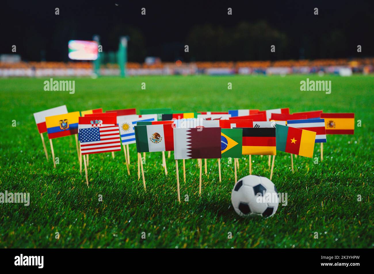National flags of Qatar, Brazil, Germany, USA and other football countries on green grass of Stadium in night. Soccer ball, black background Stock Photo
