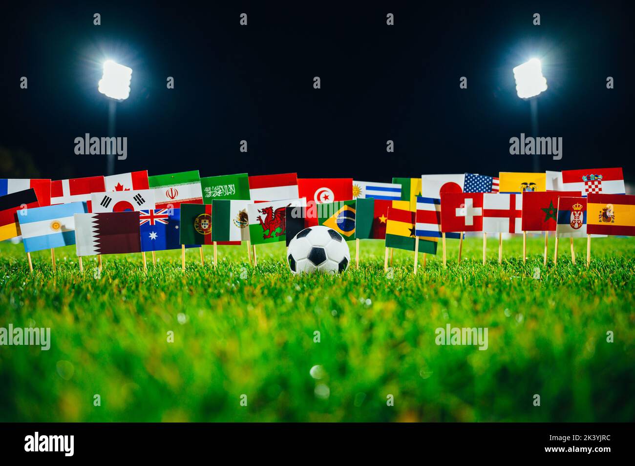 Concept photo for international football tournament. Ball on green grass and national flags. Stadium in night. Black background, edit space Stock Photo