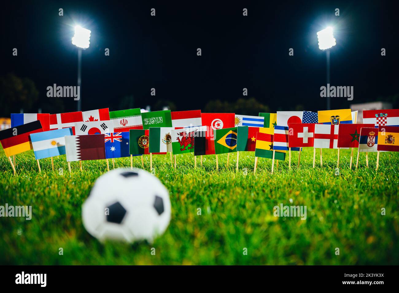 Football ball on green grass. 32 flags of all nations. Dark background, Stadium in night. Artificial light. Black edit space Stock Photo