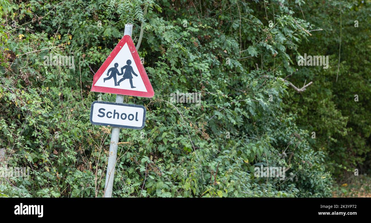 school sign in UK. Warning to slow down road sign with trees in the