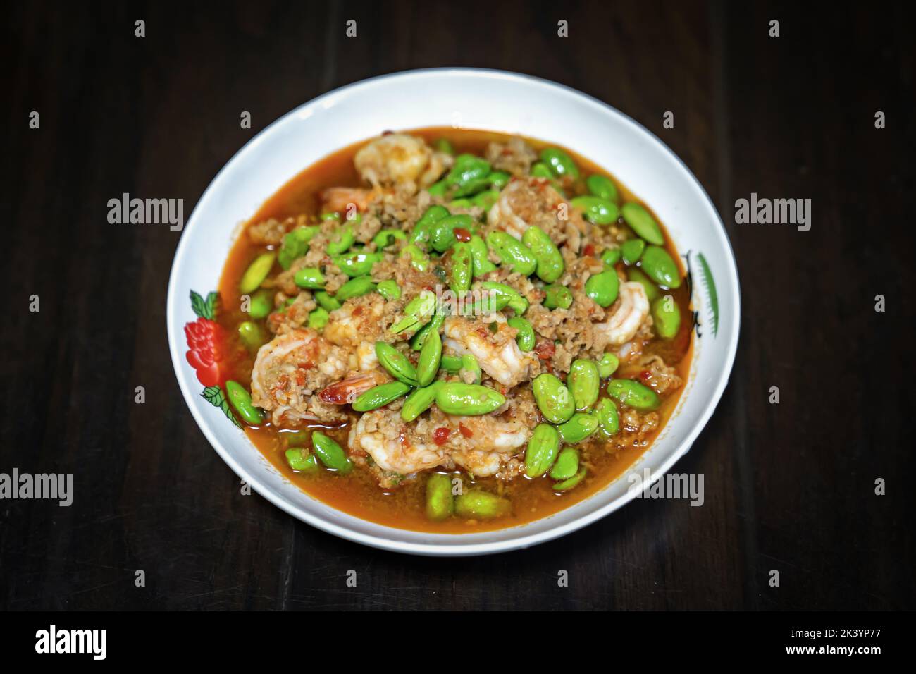 Thai Stir-Fried Stink Beans with Shrimps and spicy shrimp paste sauce in white dish bowl on dark wood table. Clipping Path. Stock Photo