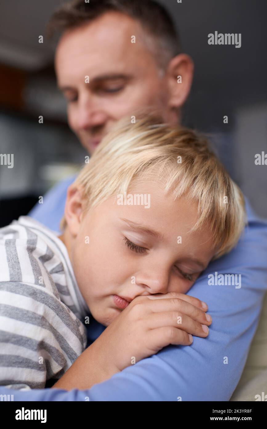 Sleeping on daddys shoulder. A mature father coming home from work and hugging his exhausted little boy. Stock Photo