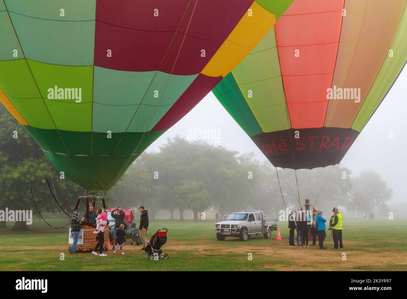 Two colorful hot air balloons on the ground on a misty day, with people