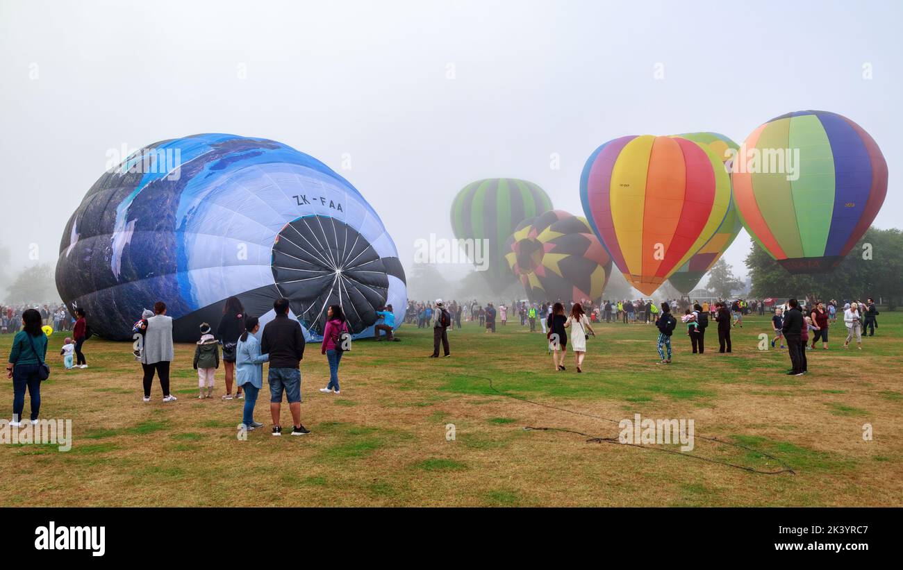 A group of hot air balloons, some only partially inflated, on a misty