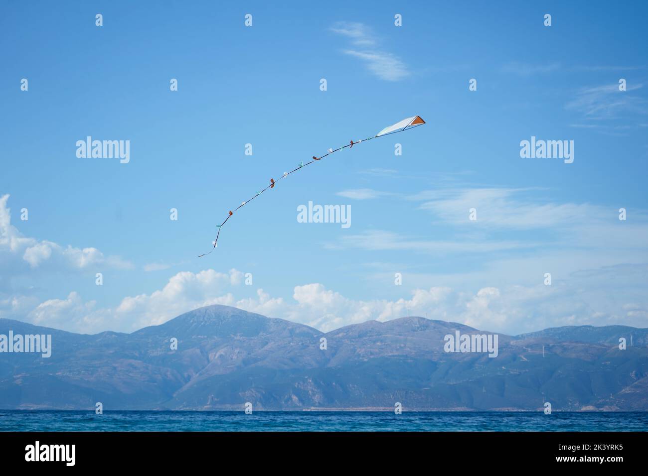 colourful kite flying in blue sky with the sea and mountains in the background Stock Photo