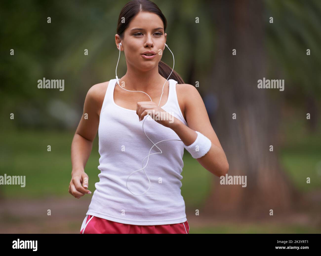 My music helps me keep the pace. A beautiful young woman jogging through a park wearing earphones. Stock Photo