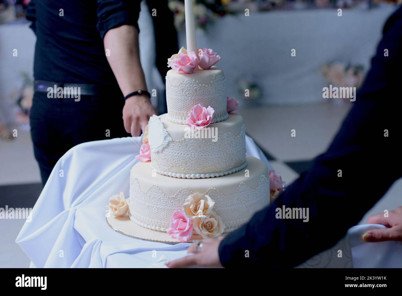 A multilevel white wedding cake with lace and pink and beige roses on top Stock Photo