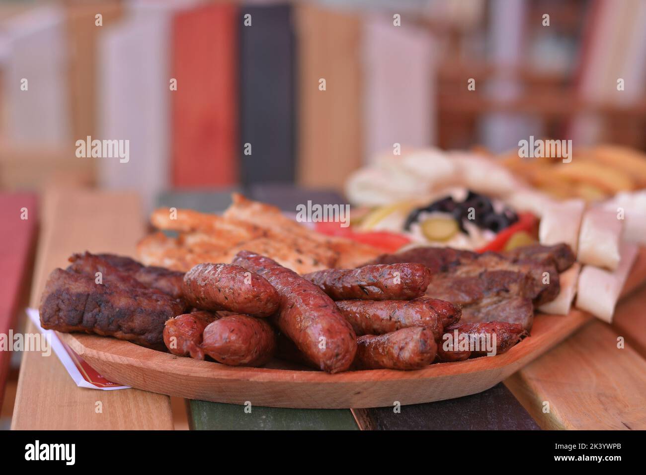 Fried sausages with herbs and grilled meat, all placed on a wooden tray. Stock Photo