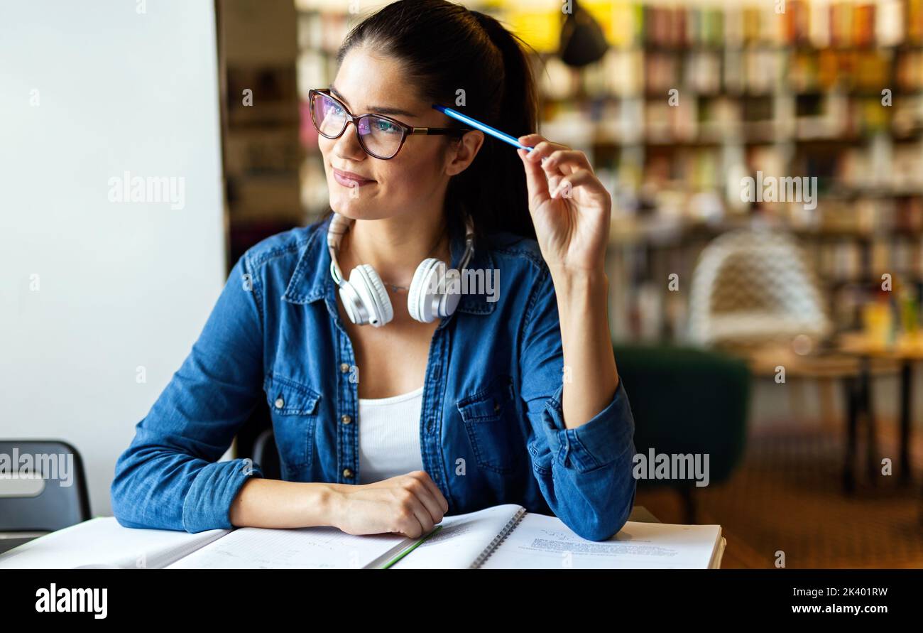 Happy young female studying and preparing for exam in college library. Education people concept Stock Photo