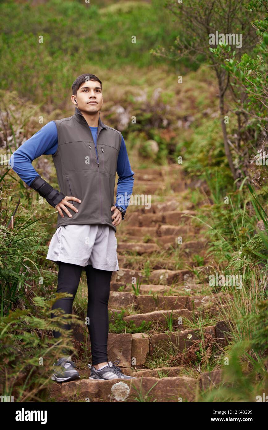 Taking a moment to catch his breath. A young runner standing on a path in the mountains. Stock Photo