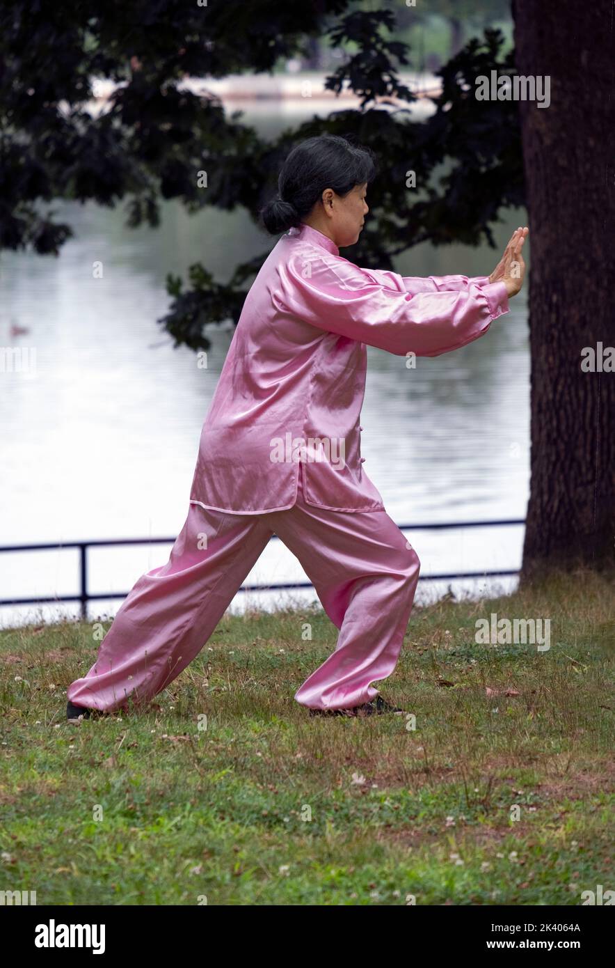 OPTICAL ILLUSION. a woman doing tai Chi in a pink robe appears to be pushing a tree which is actually farther away. in a park in Queens, New York. Stock Photo