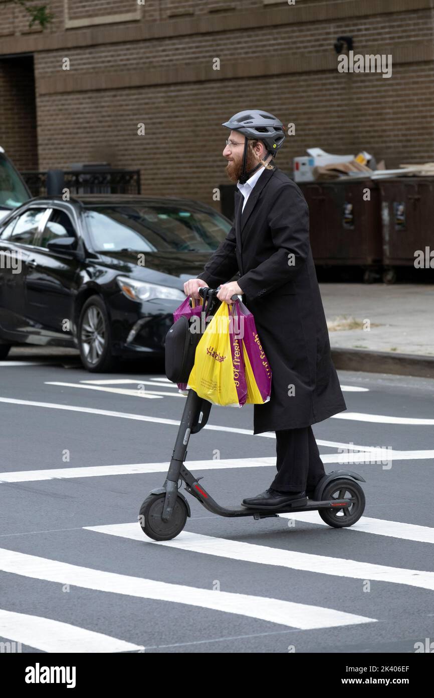 On the day before the Jewish new year an orthodox man with long peyus goes shopping and rides his electric scooter. In Williamsburg, Brooklyn, NYC. Stock Photo