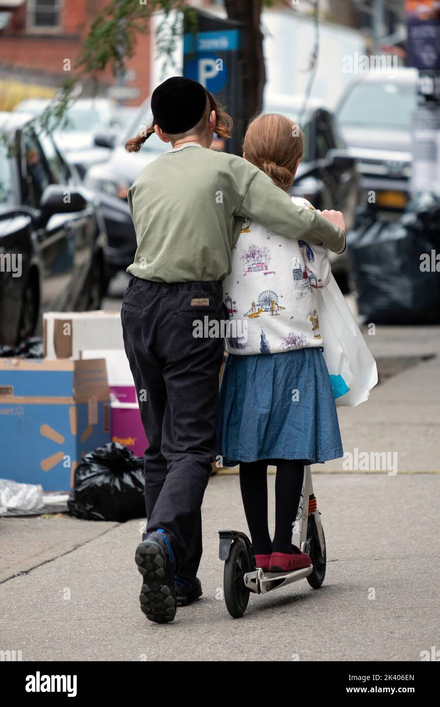 An anonymous Hasidic Jewish teenager teaches his sister how to ride a scooter. On Lee Avenue in Williamsburg, Brooklyn, New York. Stock Photo