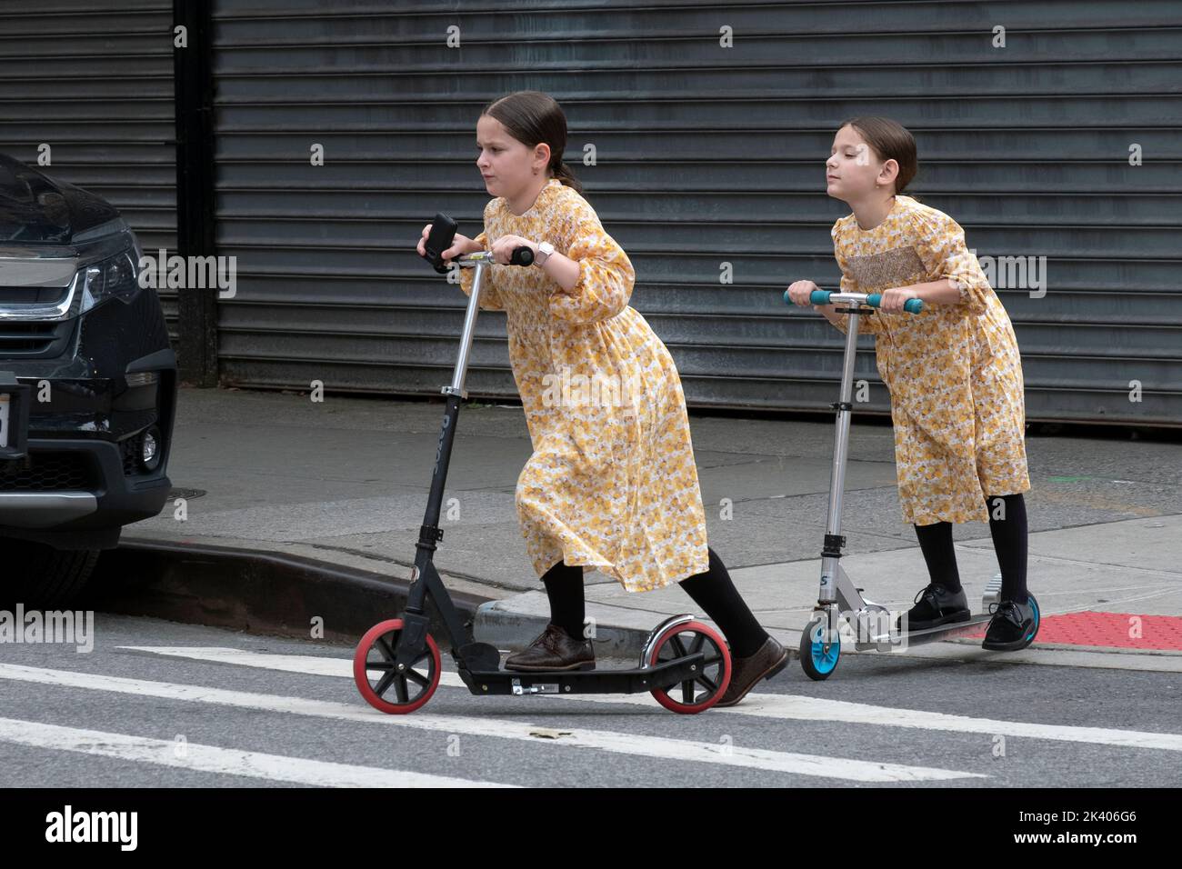 Orthodox Jewish sisters in identical dresses ride their scooters on Lee Avenue in Williamsburg, Brooklyn, New York. Stock Photo