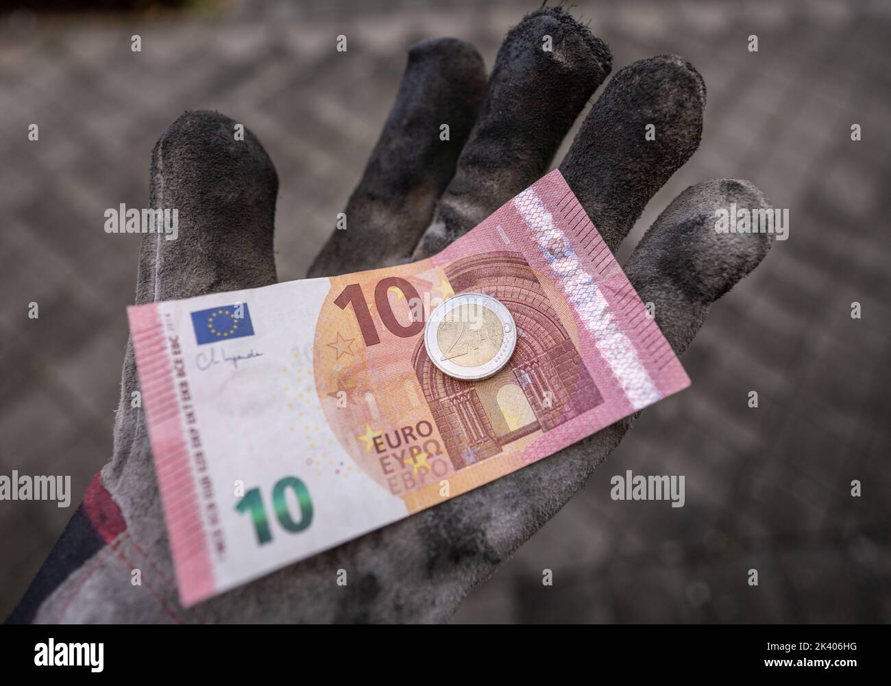 ILLUSTRATION - 28 September 2022, Hesse, Frankfurt/Main: A ten-euro bill and a two-euro coin lie in a work glove. On Oct. 1, 2022, the minimum wage in Germany will rise to twelve euros. According to a new study, 6.64 million people will then receive more money gross per hour worked. Photo: Frank Rumpenhorst/dpa Stock Photo