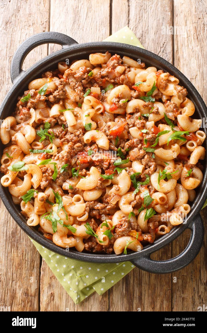 Comfort food ground beef cooked with onions, tomato sauce, and macaroni closeup in the pan on the wooden table. Vertical top view from above Stock Photo