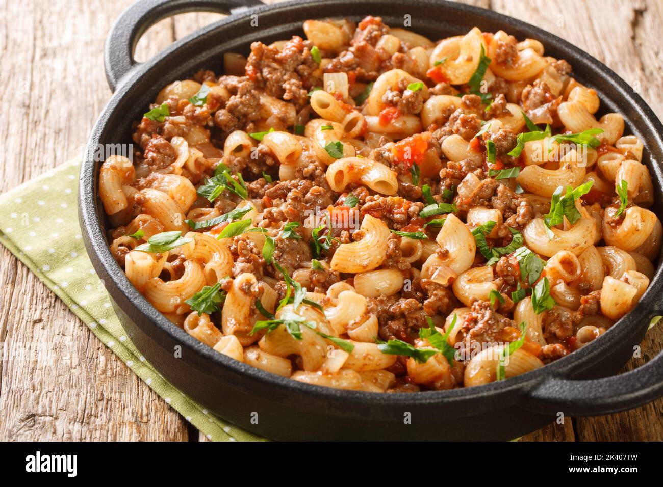 Homemade Hamburger Macaroni and Cheese with Parsley closeup in the pan on the wooden table. Horizontal Stock Photo