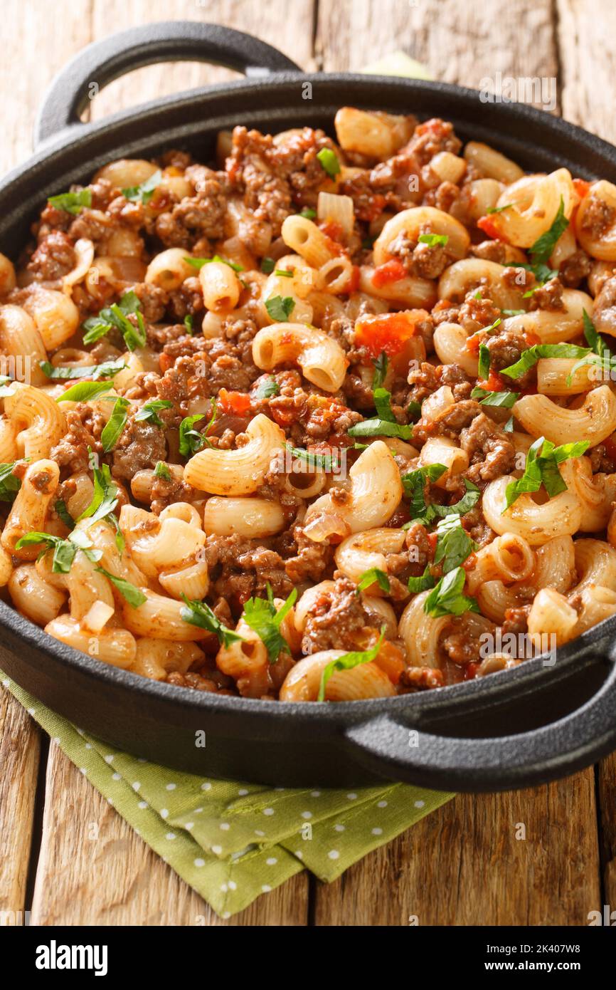 Comfort food ground beef cooked with onions, tomato sauce, and macaroni closeup in the pan on the wooden table. Vertical Stock Photo