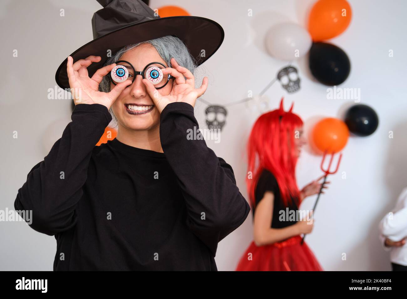 Woman dressed as witch holding eyeballs over her eyes at Halloween party. Stock Photo