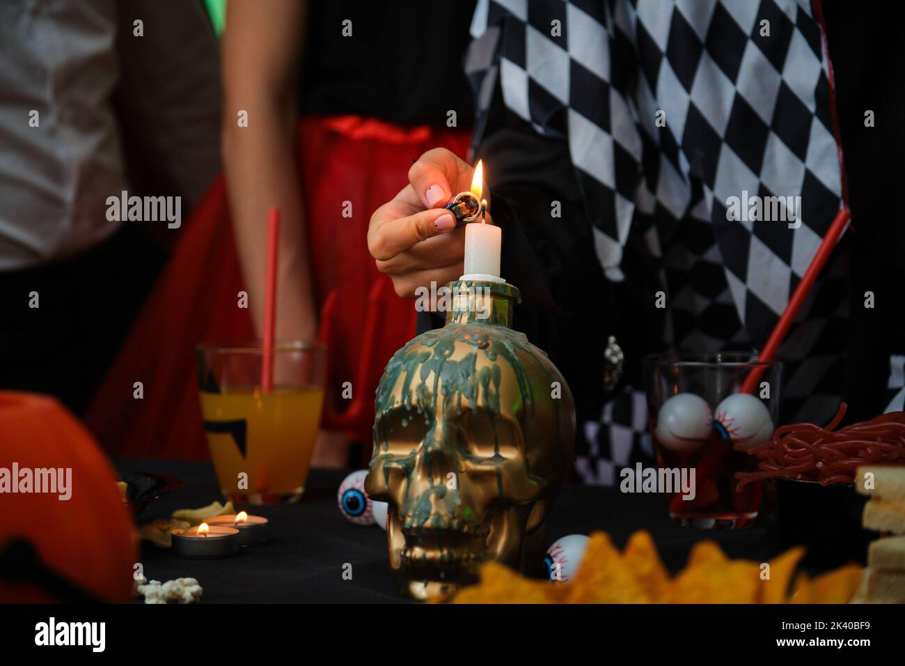 Woman lights a candle on a skull with a lighter at a Halloween party. Stock Photo