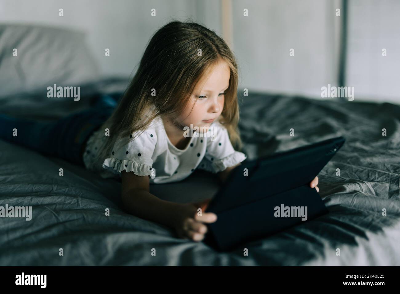 Cute little girl using digital tablet while lying in bed Stock Photo ...