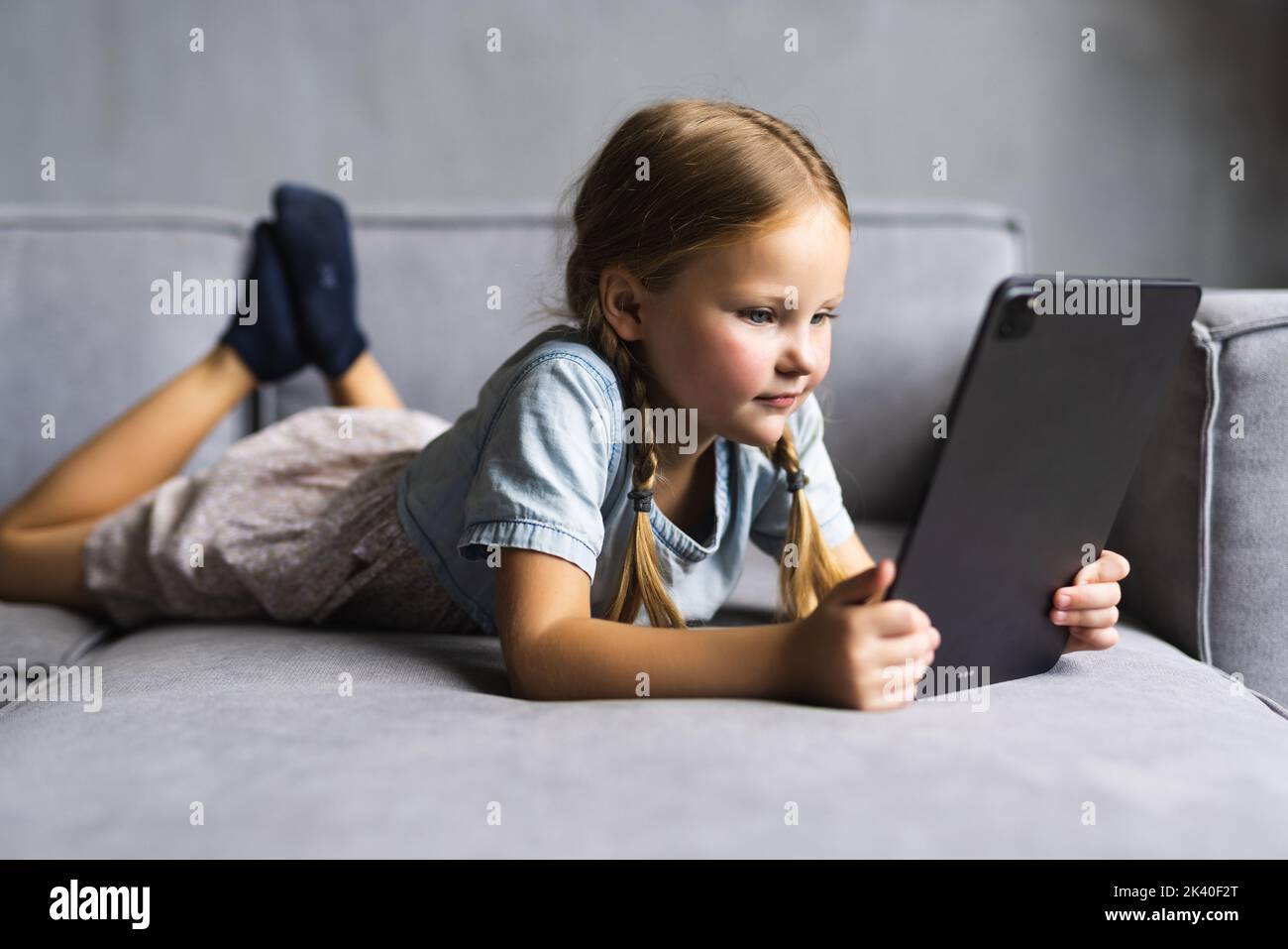 cute little girl smile lying down on sofa using looking digital tablet ...