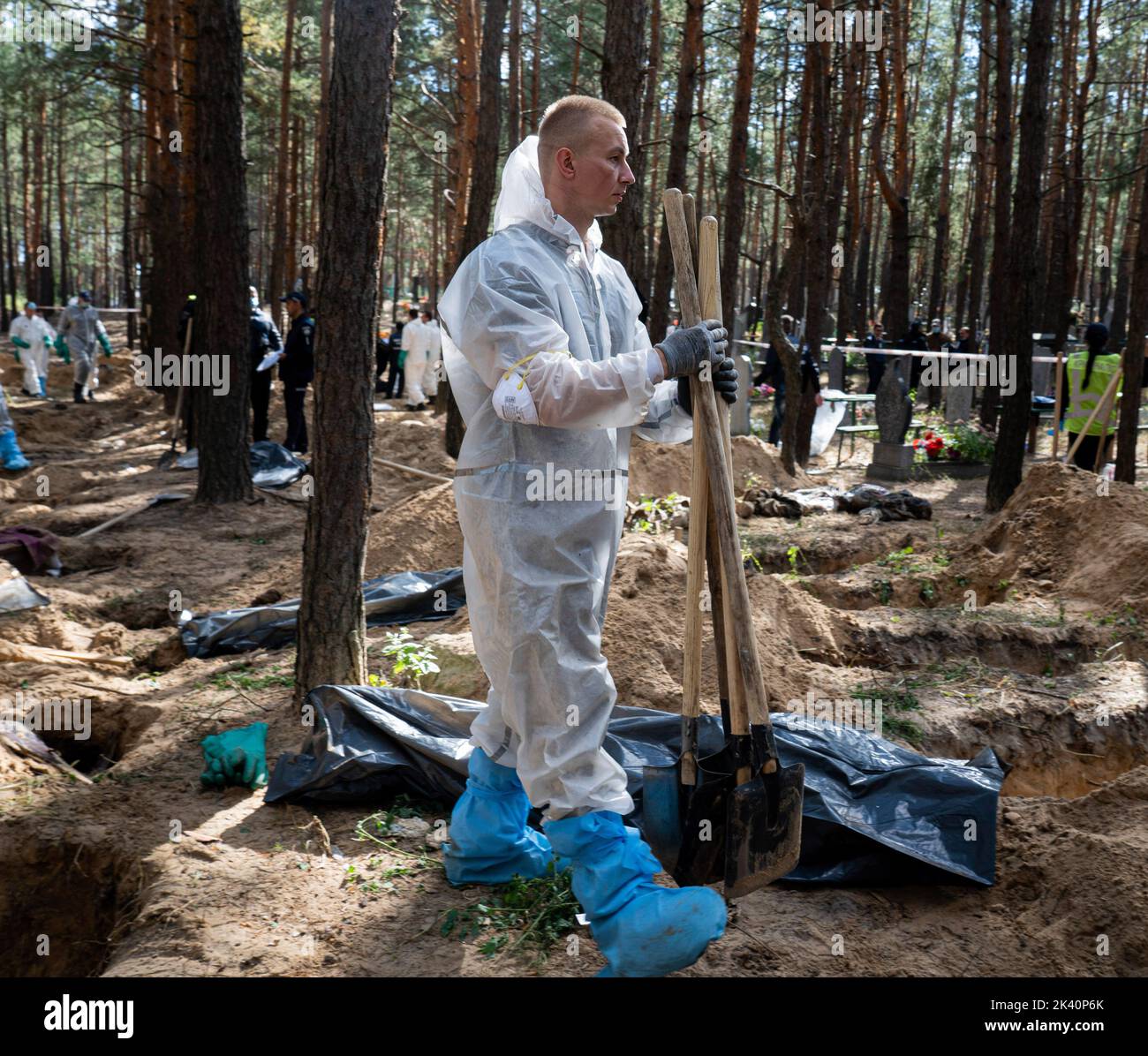 An investigator wearing protective gear is seen carrying shovels used to exhume the bodies. A mass burial site was found in the outskirt of the eastern Ukrainian city, Izyum, Kharkiv region which has been liberated from Russian occupation two weeks ago. At least 445 new graves were found in the site of an existing cemetery while many only have numbers written on the wooden cross. All bodies will be exhumed and sent for forensic examination but it was told from initial investigations that some bodies shown sign of torture. Stock Photo
