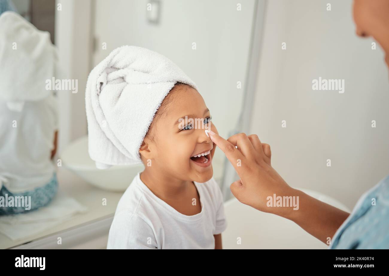 Skincare, cream and girl child at home with mother with a happy smile in a bathroom. Happiness of a kid and mom using face lotion, skin wellness and Stock Photo