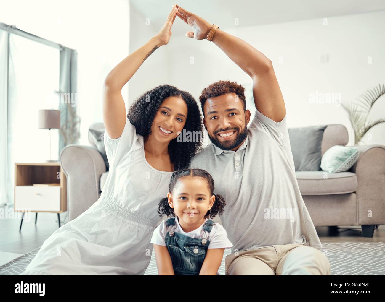 Protection, smile and portrait of family with a roof or covering hand gesture sitting on the living room floor. Happy, safety and home insurance of Stock Photo