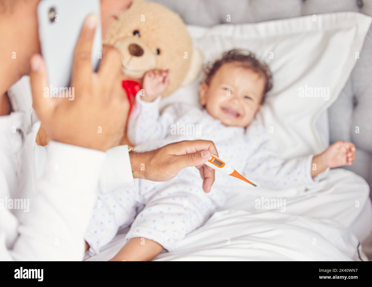 Sick child with covid or flu, mother with thermometer in hand and calling doctor for crying child. Kid with bad fever, may go to hospital or clinic Stock Photo