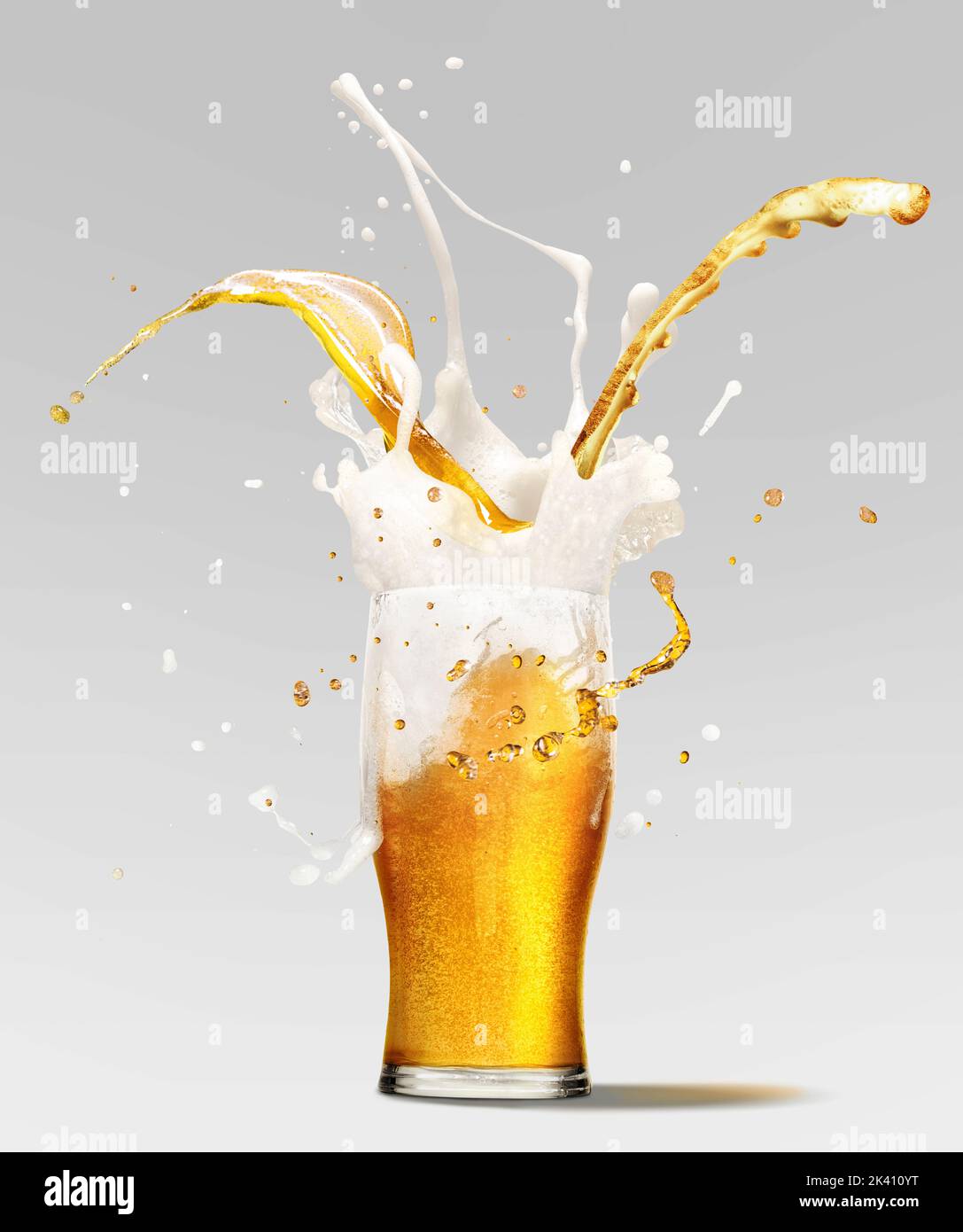 Foam splashes from full glass of frothy light lager beer isolated over light background. Concept of alcohol, oktoberfest, drinks, holidays and Stock Photo
